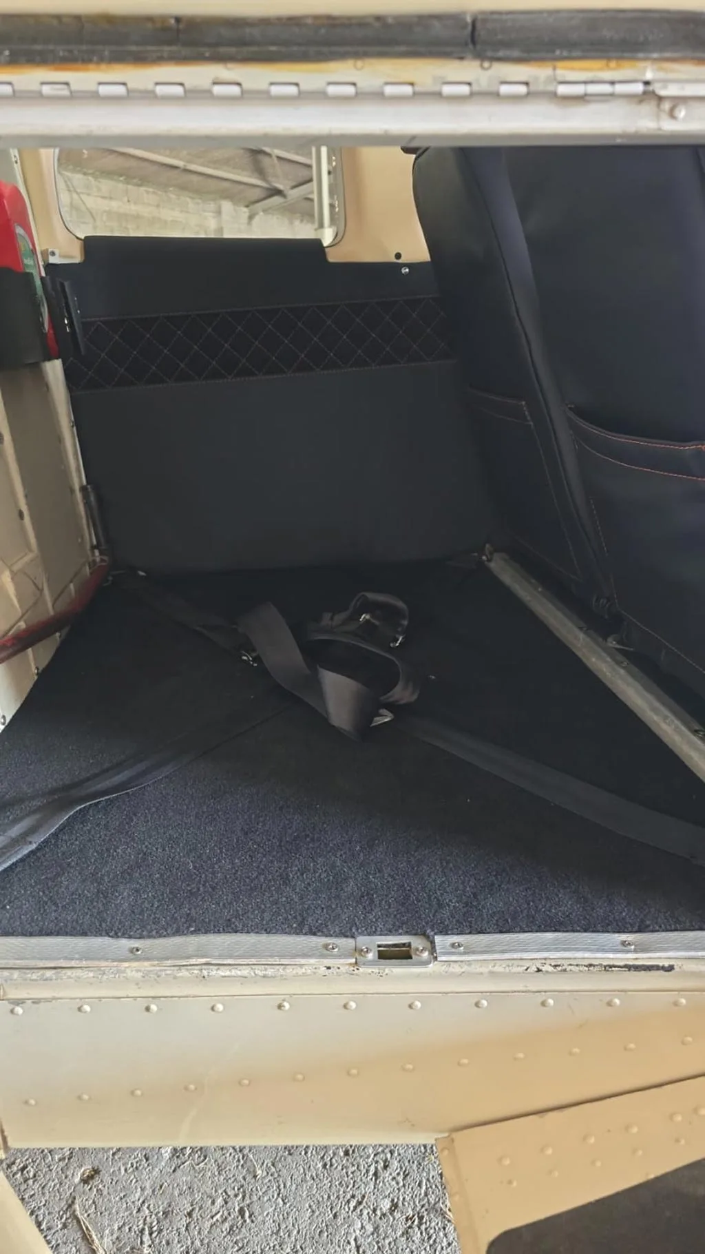 The rear baggage area of an aircraft cabin with black carpet and seatbelts.