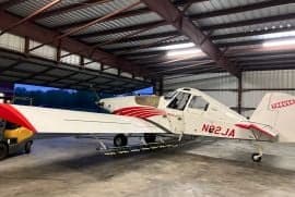 Side view of a white and red Air Tractor crop duster with tail number N92JA inside a hangar.