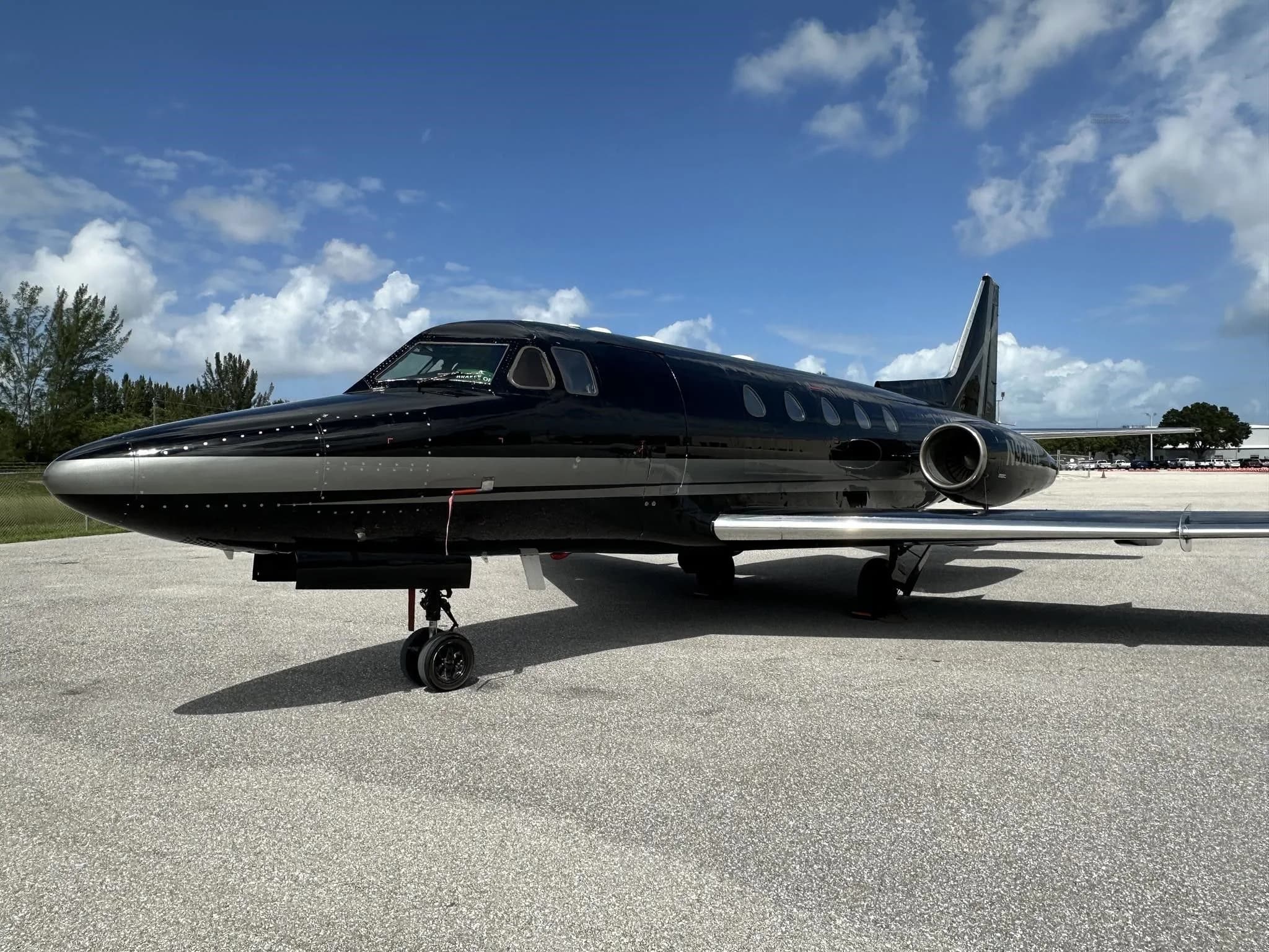 A close-up side view of the front section of a black and silver business jet parked on an asphalt tarmac.