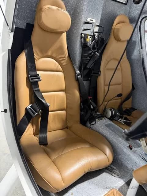 The interior of a light sport aircraft, featuring two tan leather seats with black harnesses.