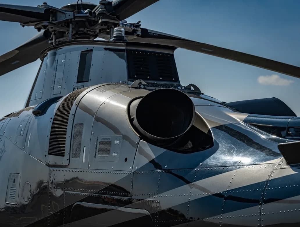 A close-up view of the engine exhaust and rotor mast of a grey AgustaWestland AW109 GrandNew helicopter with striped livery.