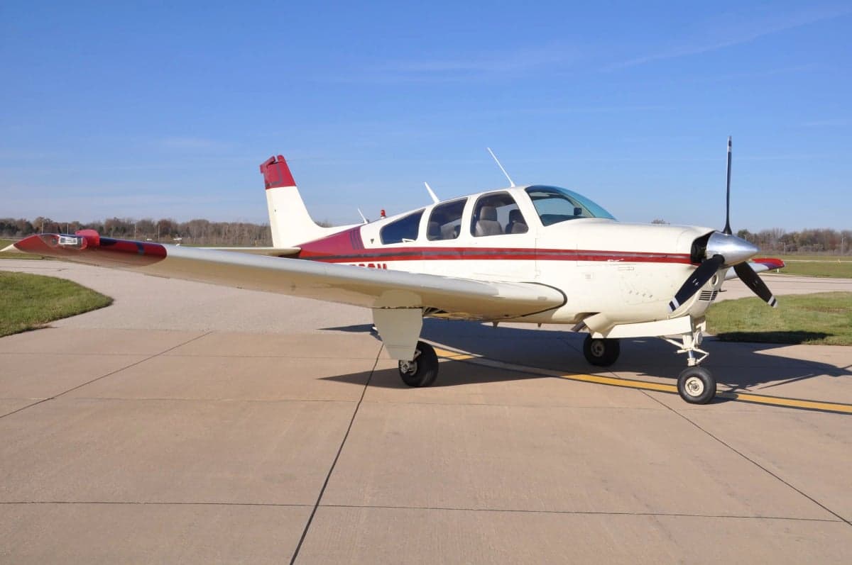 Side view of a Beechcraft Bonanza with a red and white paint scheme on the tarmac.