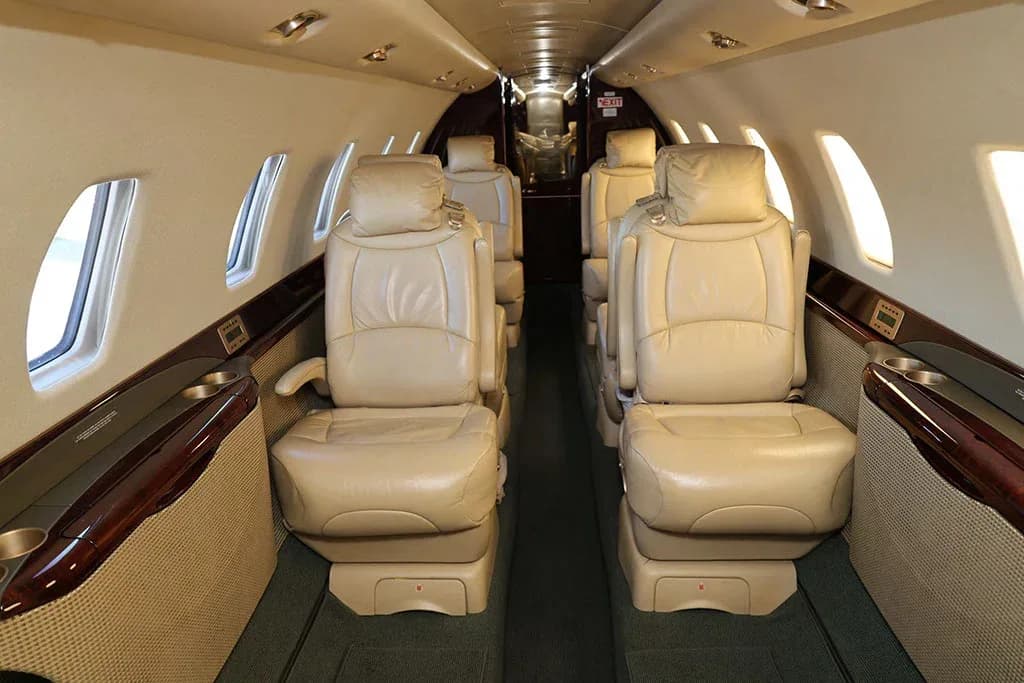 The interior cabin of a private jet with beige leather seats arranged in a club configuration, facing each other.