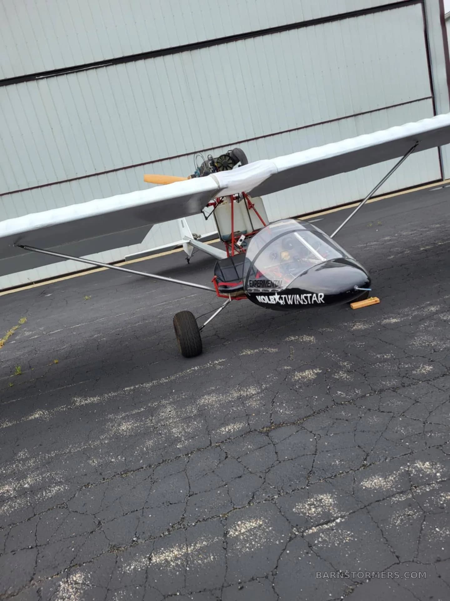 A black and white Volmer VJ-24W SunFun experimental aircraft is parked on an asphalt ramp next to a hangar.