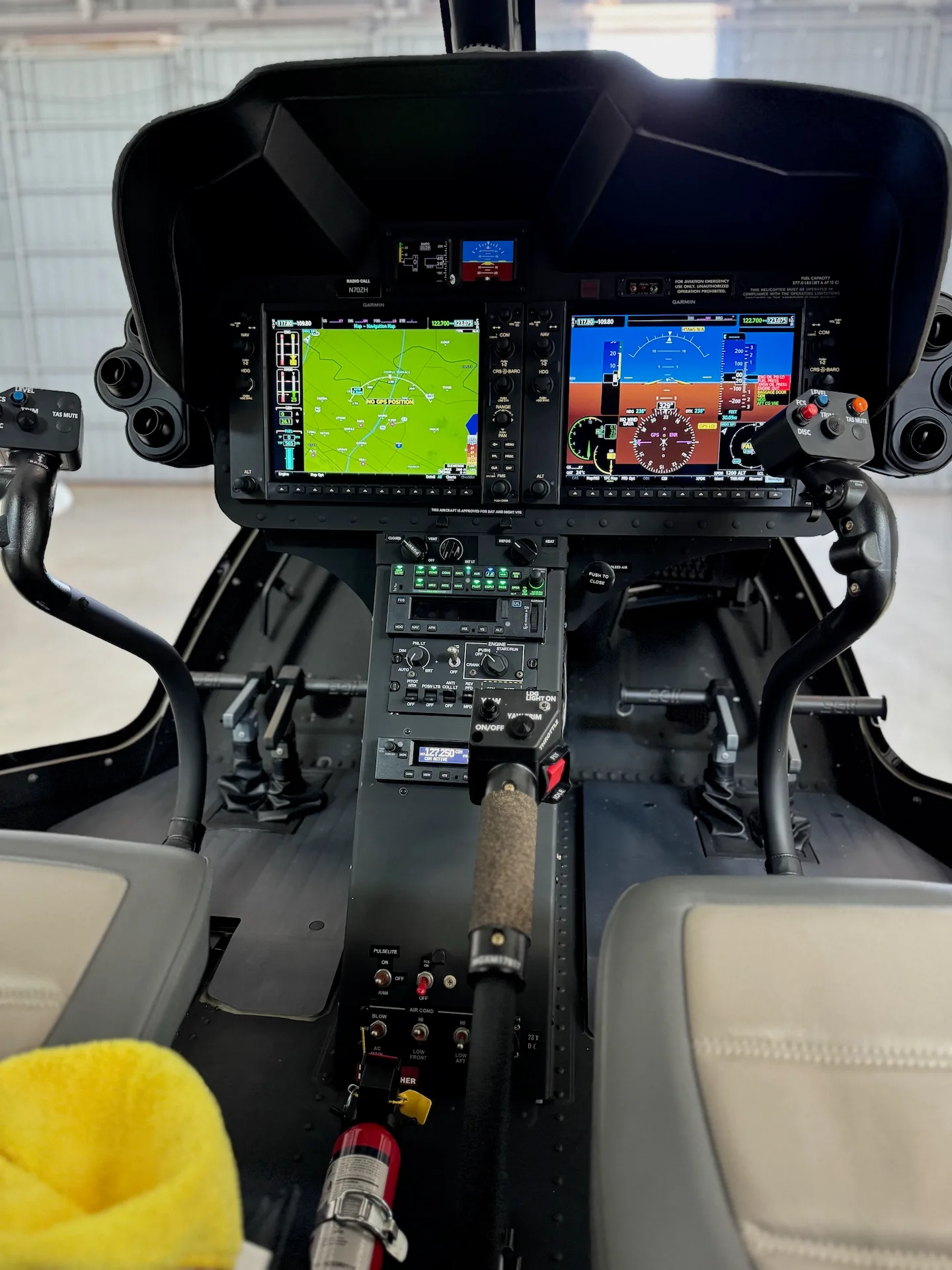 The cockpit of a helicopter with two large digital displays and various controls.