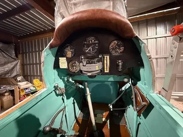 The cockpit of a vintage aircraft with a brown padded coaming and a black instrument panel with several gauges.