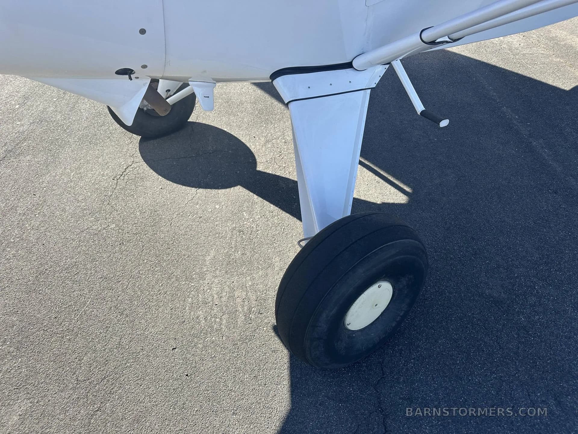 A close-up view of the main landing gear and tire of a white Maule M-7-235 aircraft, showing the wheel hub.