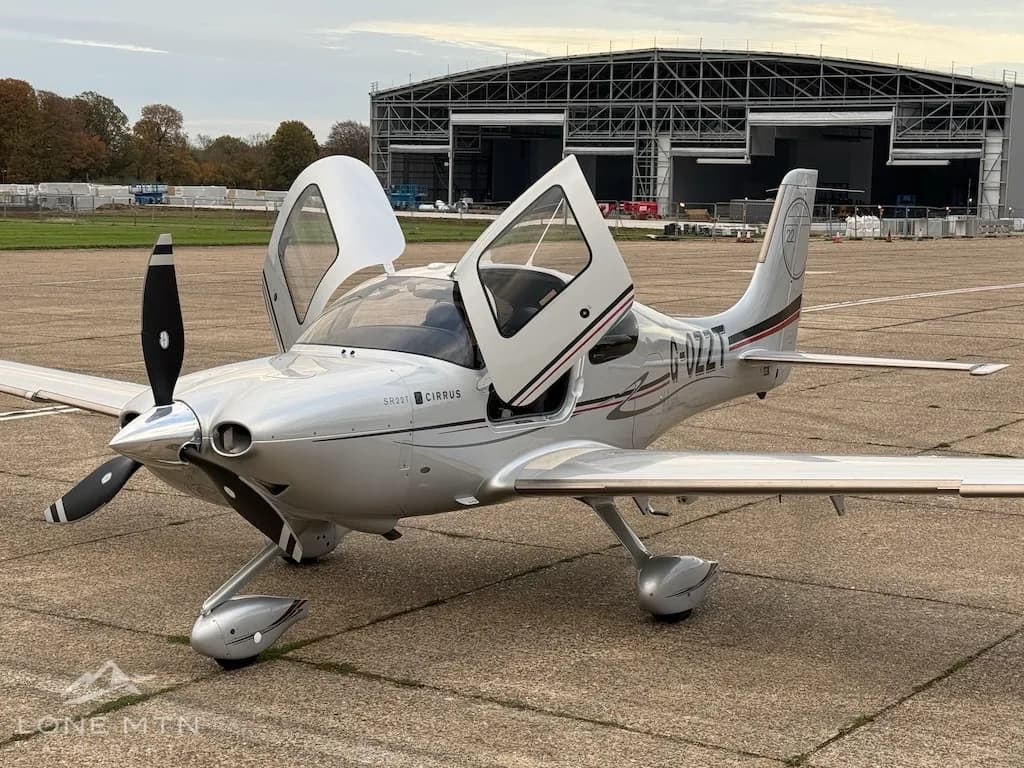 A silver Cirrus SR22T aircraft with open doors parked on an airfield tarmac.