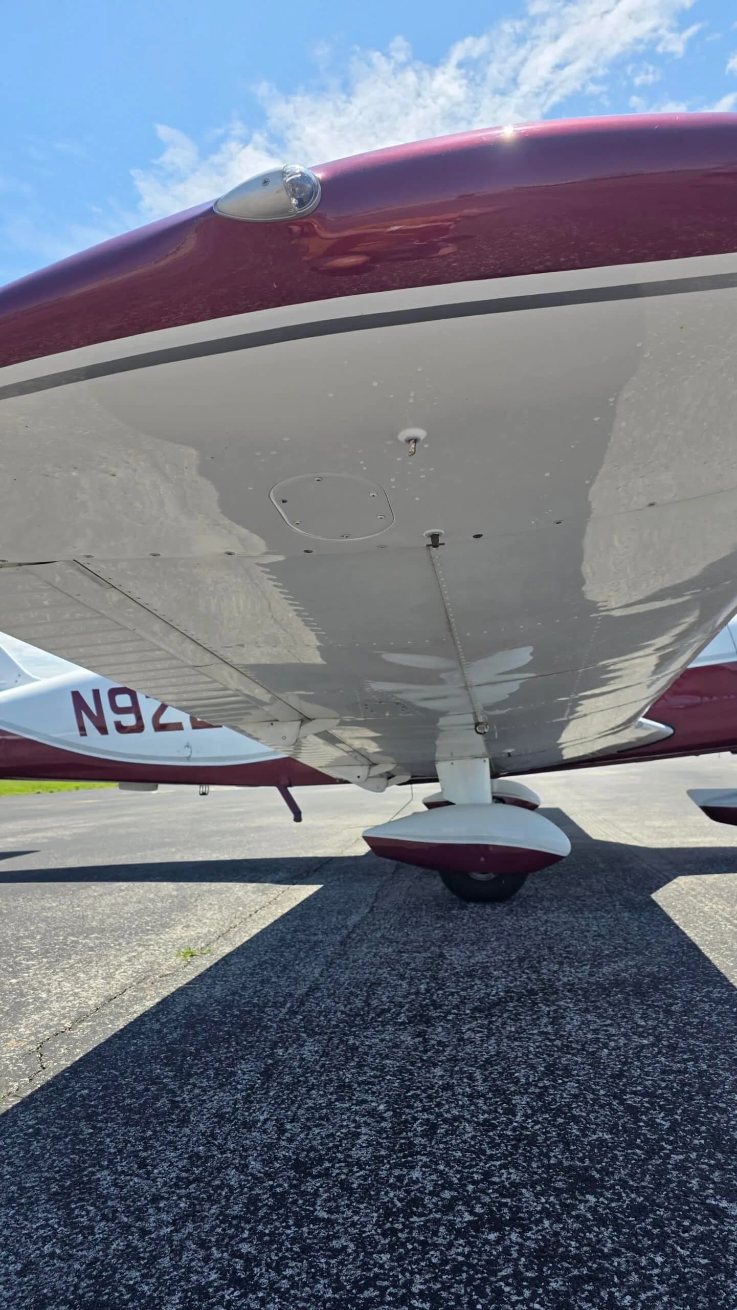 An underside view of the right wing and landing gear of a white and maroon Piper Cherokee (N9221W).