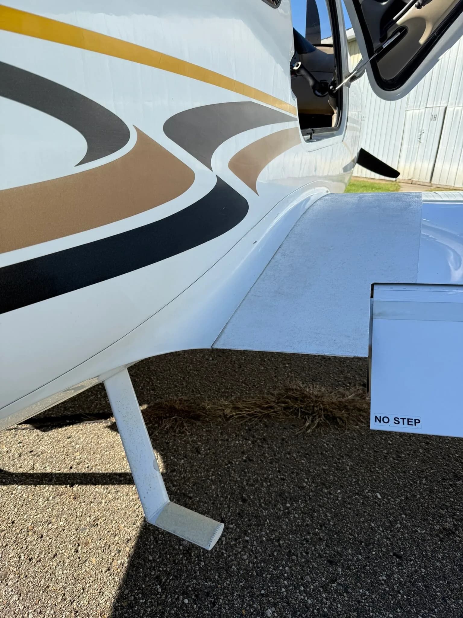 A close-up view of the white fuselage and wing root of the Cirrus SR20, showing the black and gold stripe detail and a step.