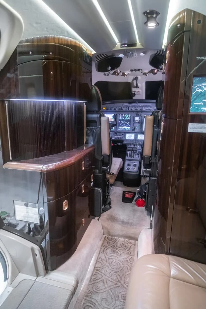 The luxurious interior of an aircraft cabin with tan leather seats and a wooden table.