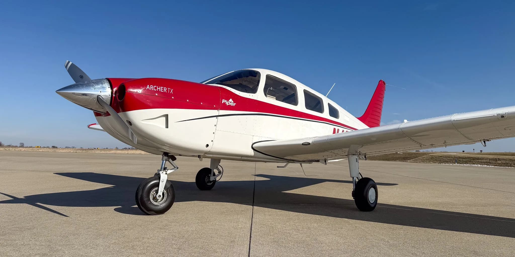 A low-angle front view of a white Piper Archer TX with red accents and tail number N424TF on an airfield.