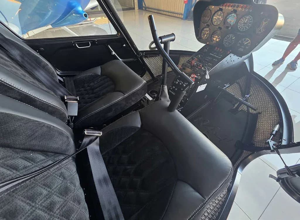The cockpit of a helicopter with black quilted seats, cyclic stick, and a classic instrument panel.