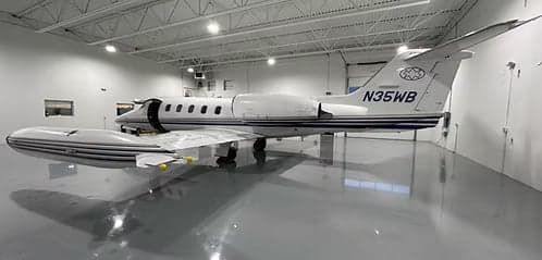 A Learjet with tail number N35WB parked in a hangar with an open door.