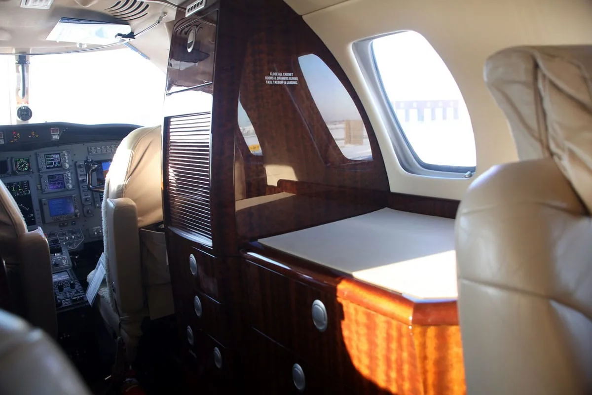 A view inside the private jet cabin, showing a polished wood cabinet and a glimpse of the cockpit instruments.