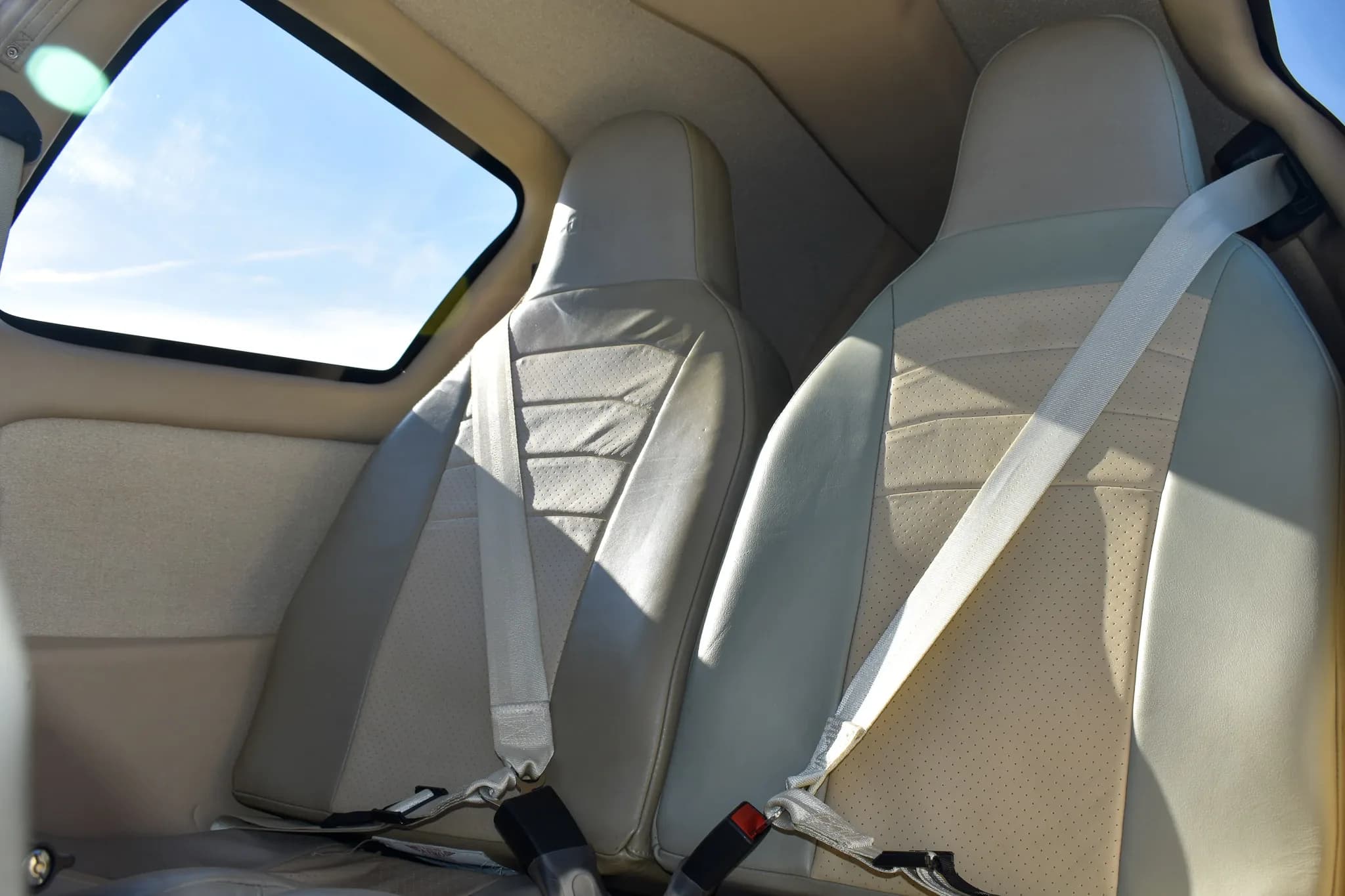 Two light-colored leather seats with seatbelts in the aircraft's cabin.