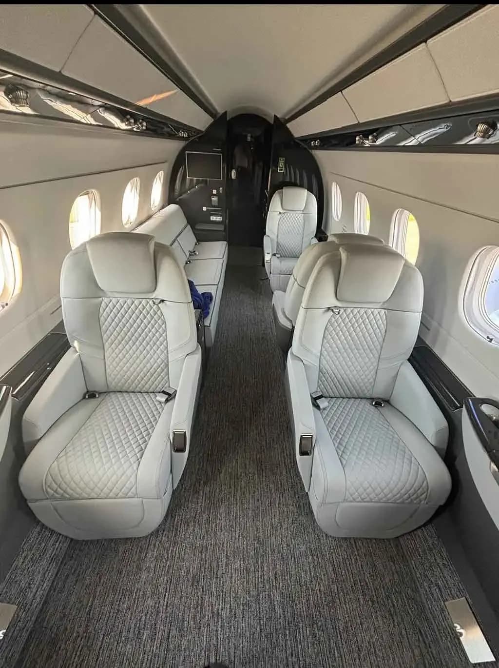 The luxurious cabin interior of a business jet, featuring light grey quilted leather seats and a dark grey carpet.