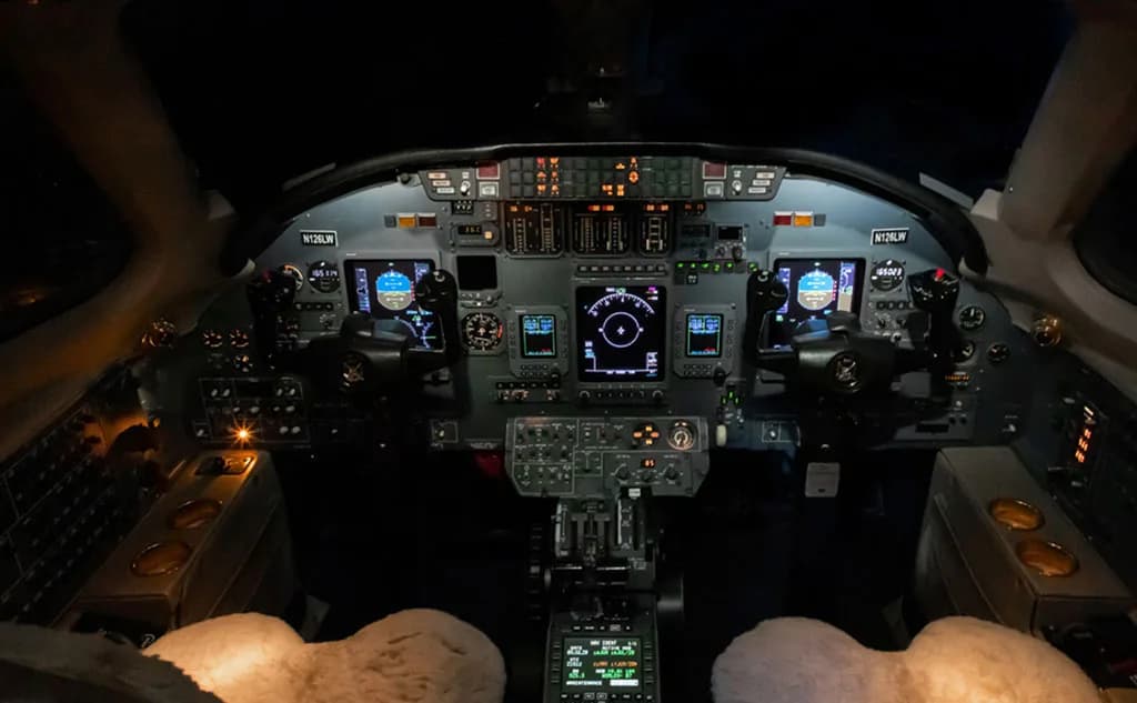 The illuminated cockpit of a private jet, showing multiple digital displays and control panels.