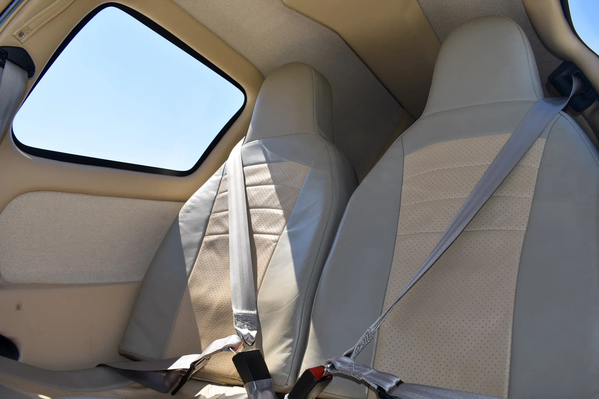 Interior view of two light-colored leather seats with seatbelts in the aircraft cabin.