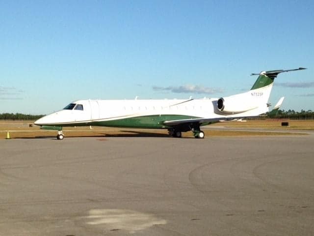 An Embraer Legacy 650 with green and white paint scheme parked on the tarmac.