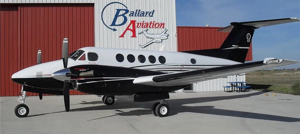 Side view of a King Air aircraft with a black and white paint scheme parked outside a hangar.