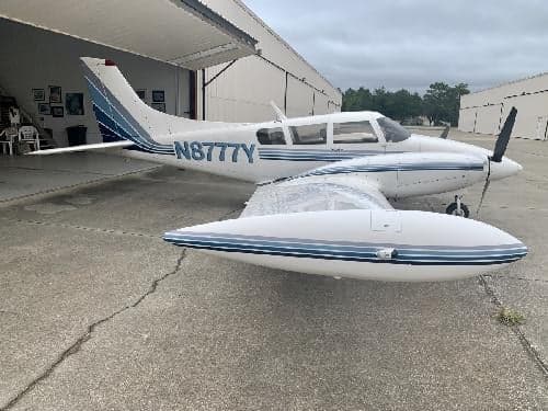 A Piper Aerostar aircraft with blue stripes is parked in front of a hangar.