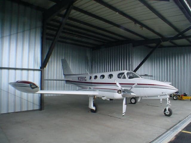 A white twin-engine aircraft with red and grey stripes, registration N3911G, parked inside a metal hangar.