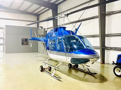 A blue and white Bell 407 helicopter parked in a hangar.