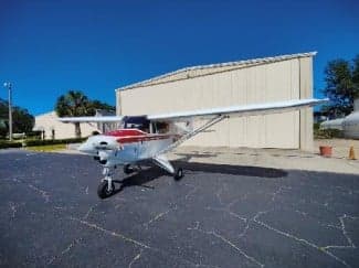 A white and red aircraft is parked on the tarmac in front of a hangar.
