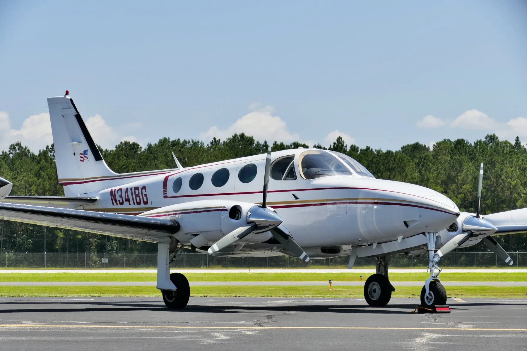 Side view of a white twin-engine propeller aircraft N341BG with red and gold stripes on an airfield.