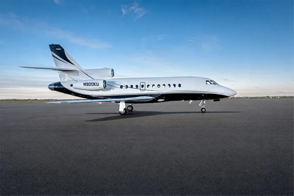 A Dassault Falcon 900EX business jet, registration N900KU, parked on a tarmac under a blue sky.