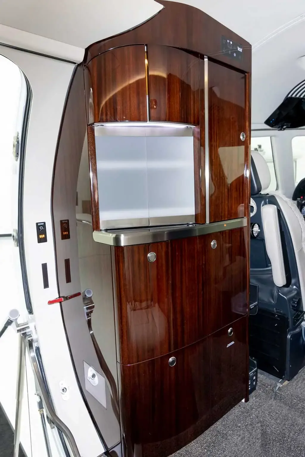A dark wood-paneled galley cabinet with a silver counter and storage compartments is visible inside the private jet cabin.