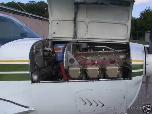 The engine compartment of a white and green aircraft with the cowling open, revealing the engine.