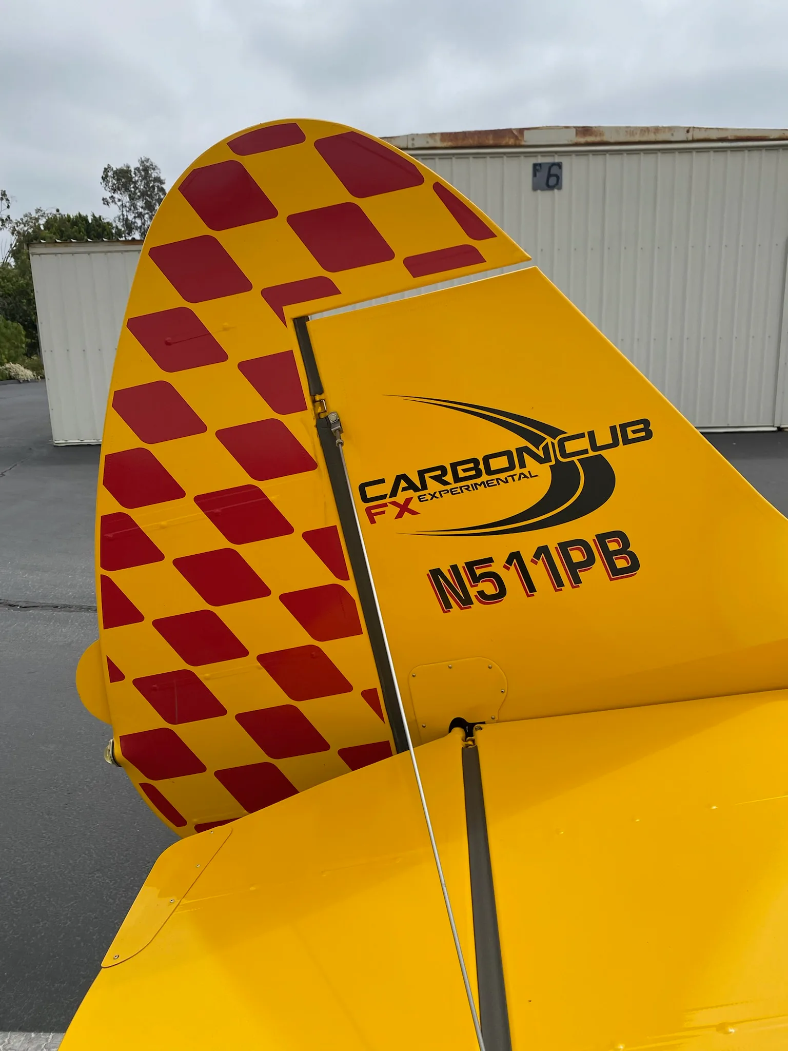 Tail of a yellow Carbon Cub aircraft with red checkered pattern and N number.