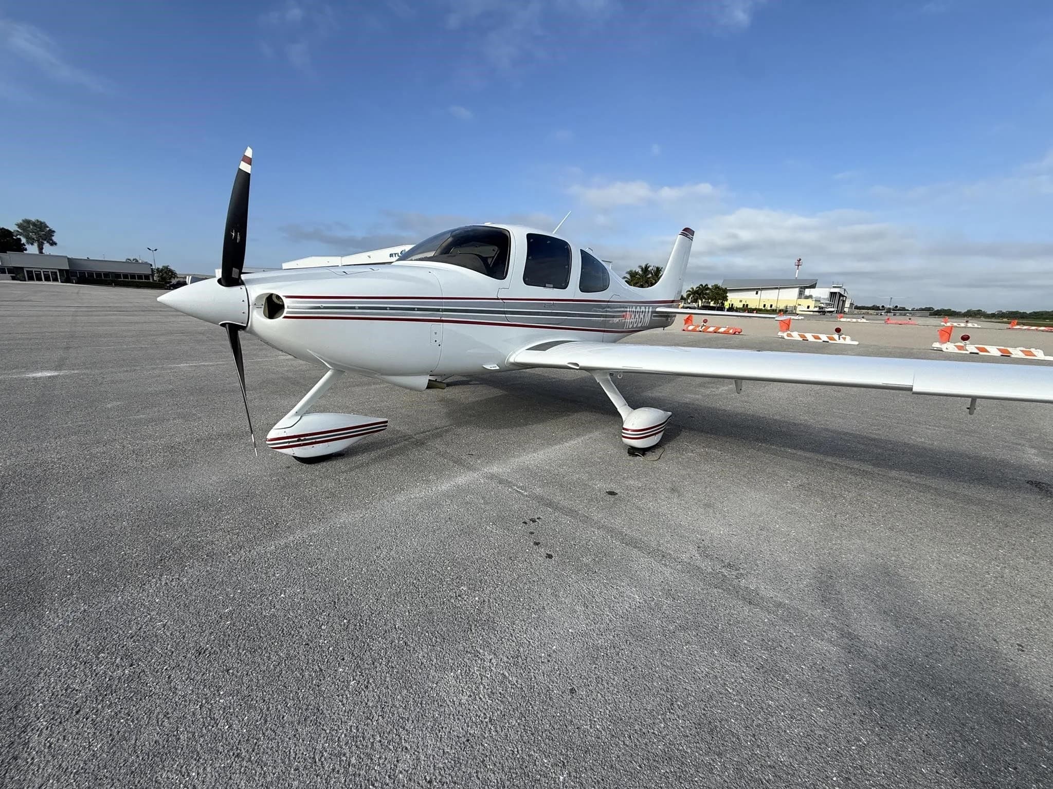 A front-left view of a white Cirrus SR22 aircraft with red and gray stripes, tail number N88BM, parked on an airport tarmac.