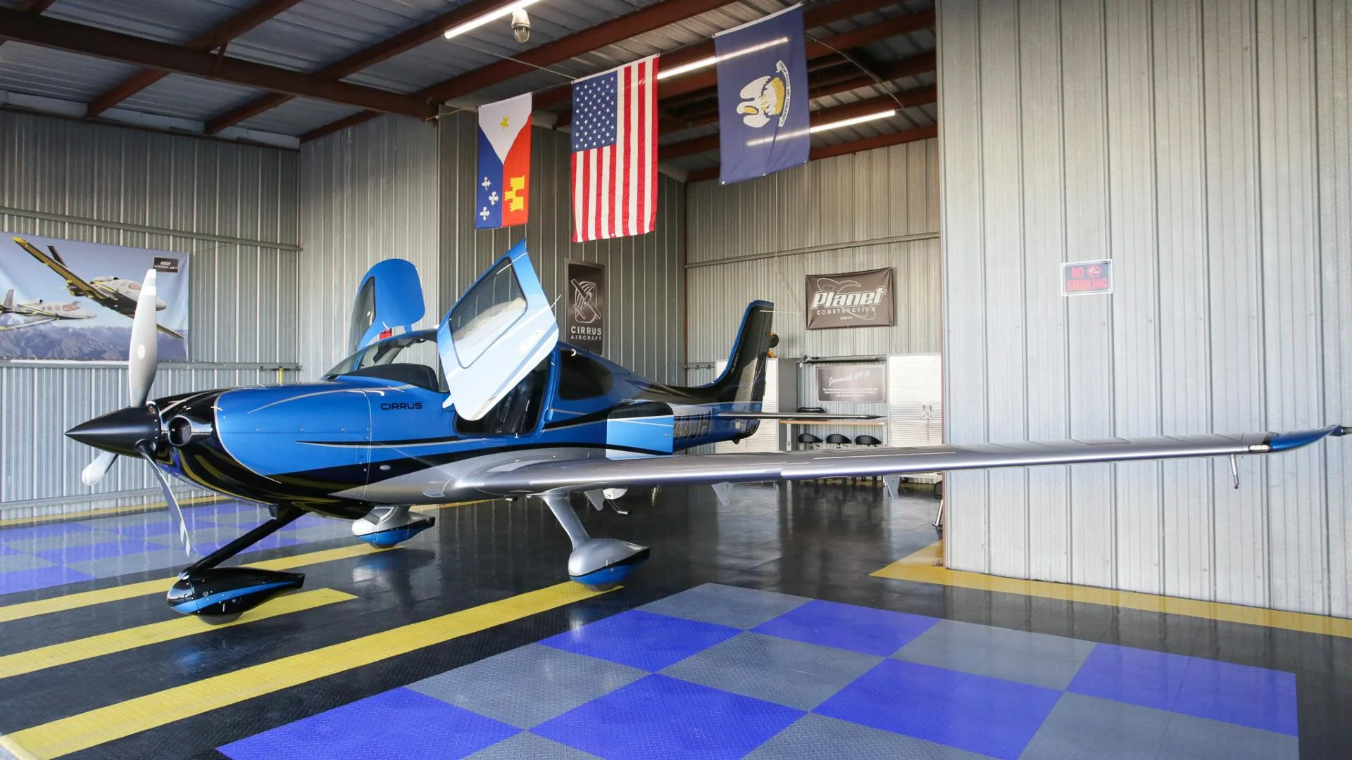 A blue and silver Cirrus SR22 aircraft with registration N444JH parked inside a hangar with its doors open.
