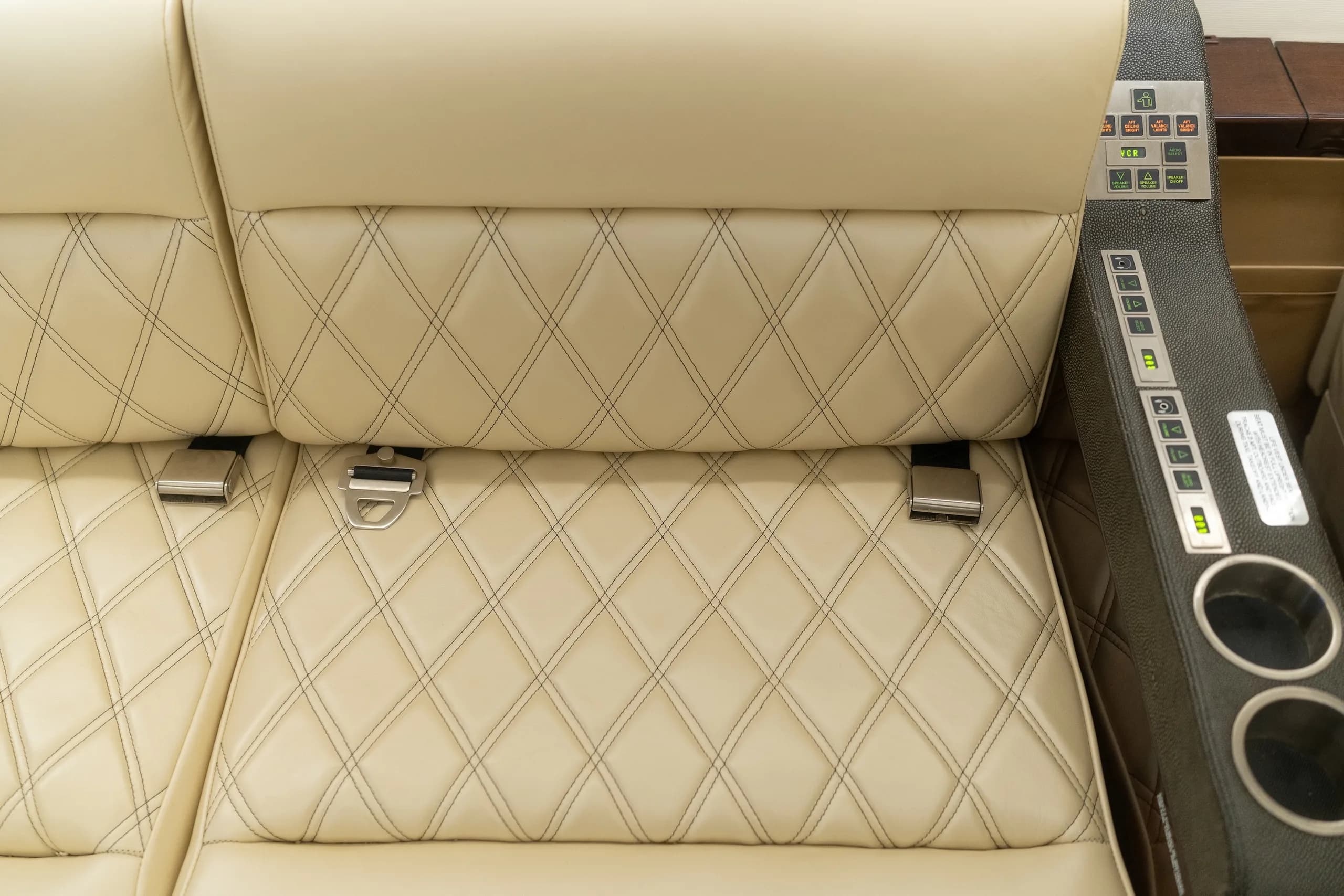 Close-up of cream-colored quilted leather aircraft seats with seatbelts and an armrest console.