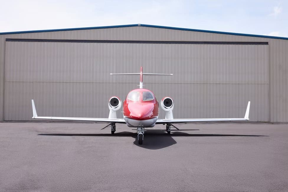 Front view of a red and white HondaJet parked in front of a hangar.
