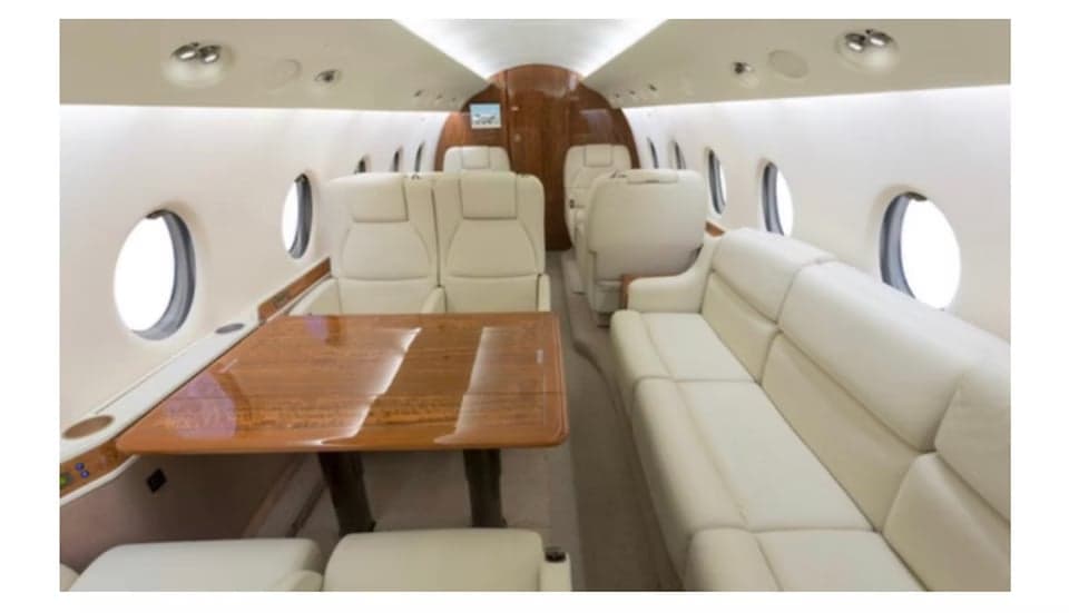 The aircraft's interior features white leather seats and a wooden table.