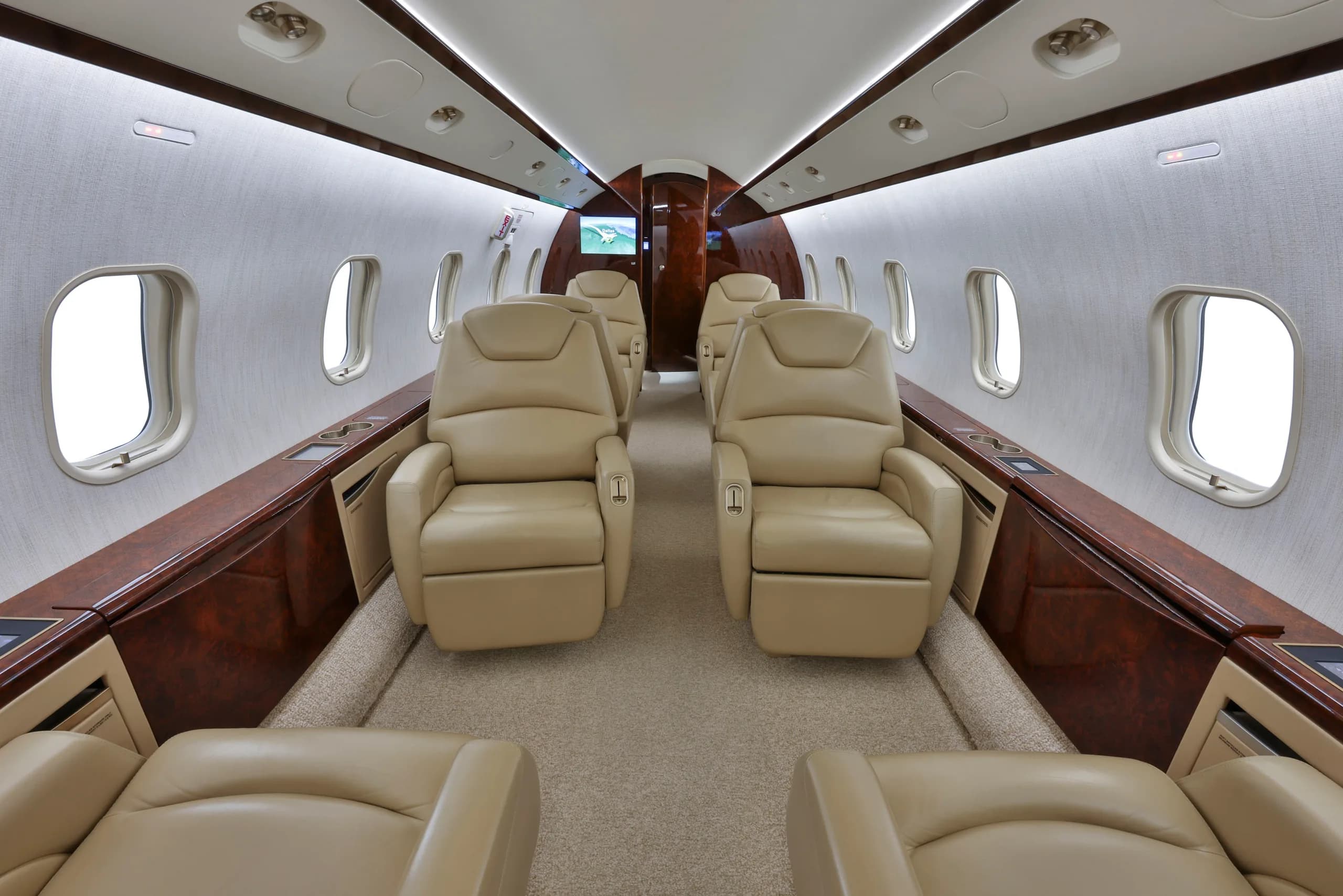 The luxurious interior cabin of a business jet with tan leather seats and dark wood accents.