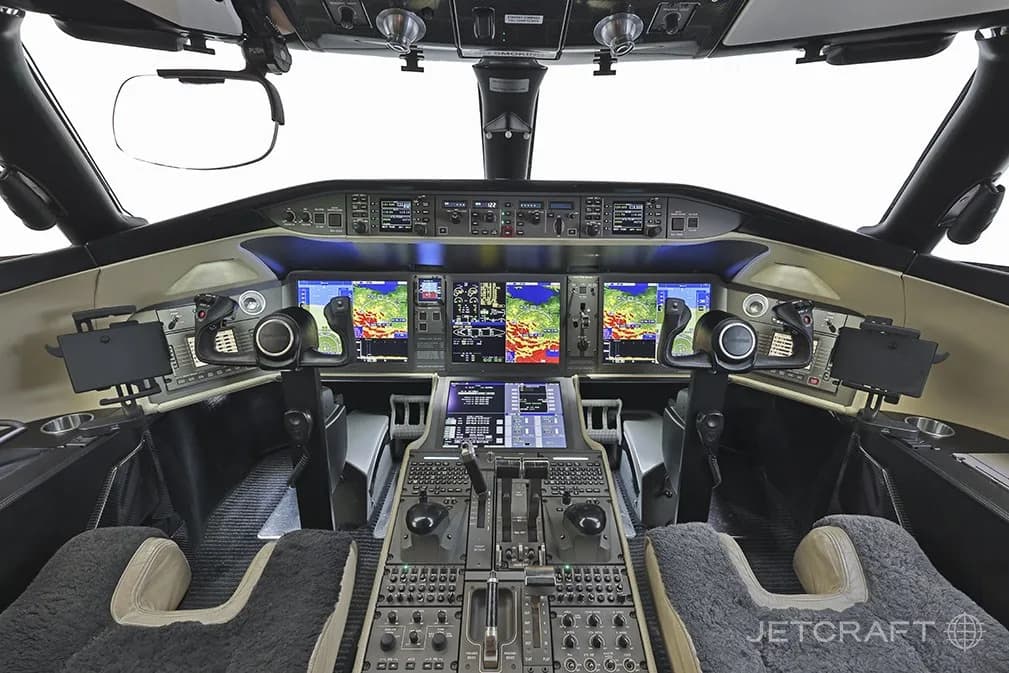 The modern cockpit of a Bombardier Global 6000 business jet with multiple large display screens showing flight information and maps.