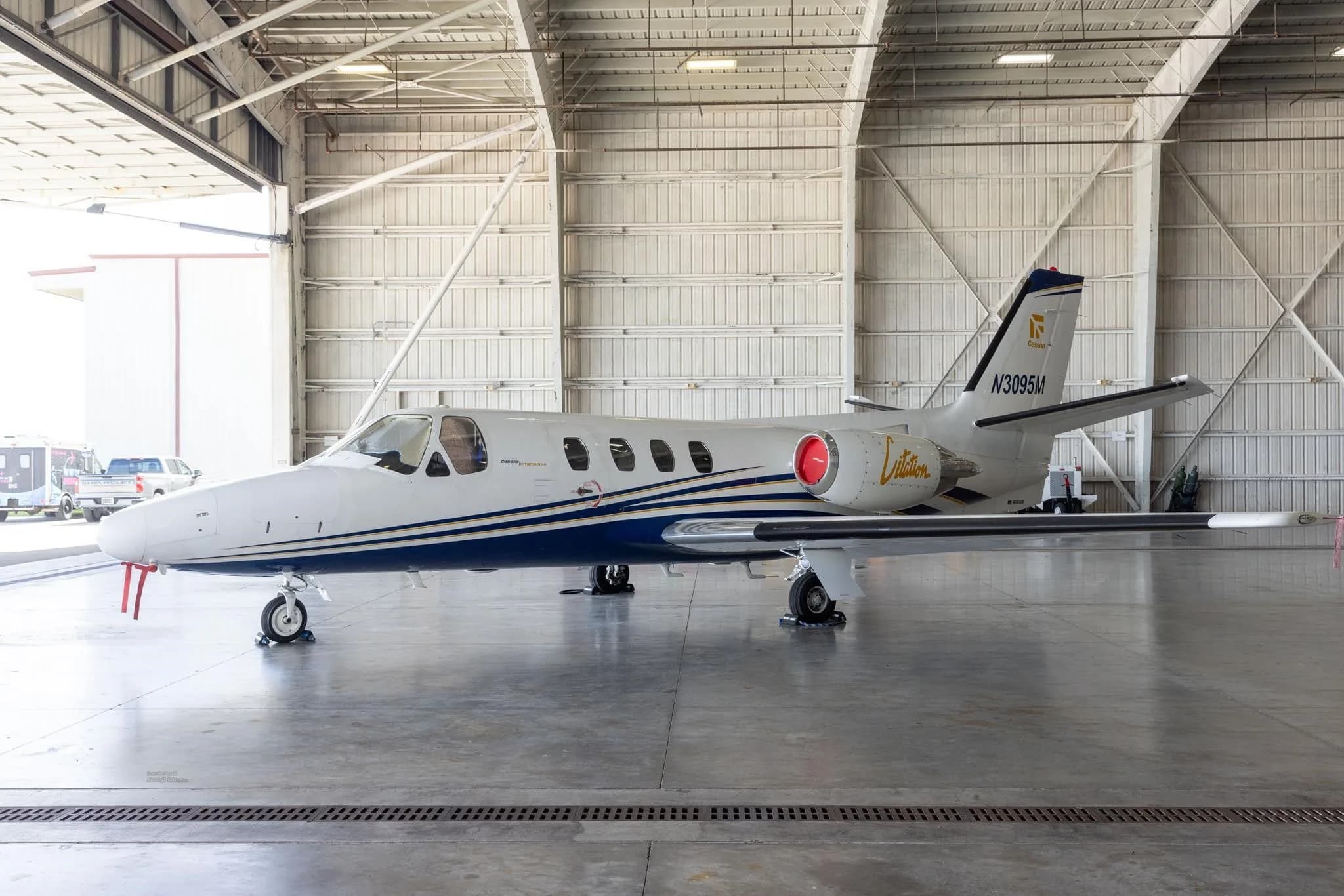 A side view of the white and blue Cessna Citation jet (N3095M) parked inside a hangar.