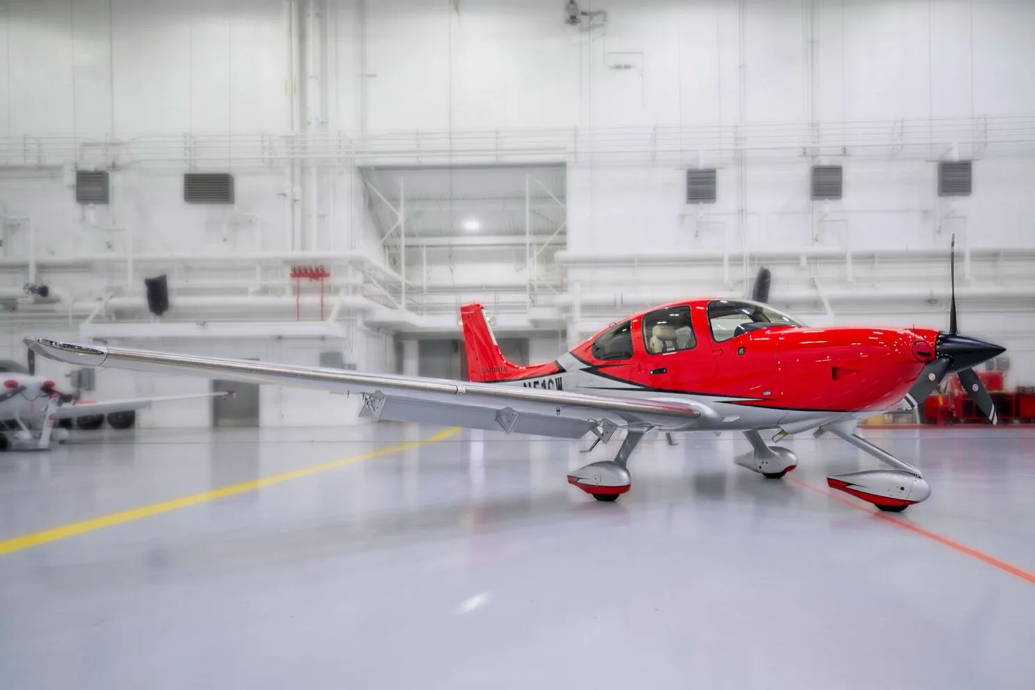 A red and white Cirrus SR22 aircraft with registration N51CW parked in a hangar, with another aircraft visible in the background.