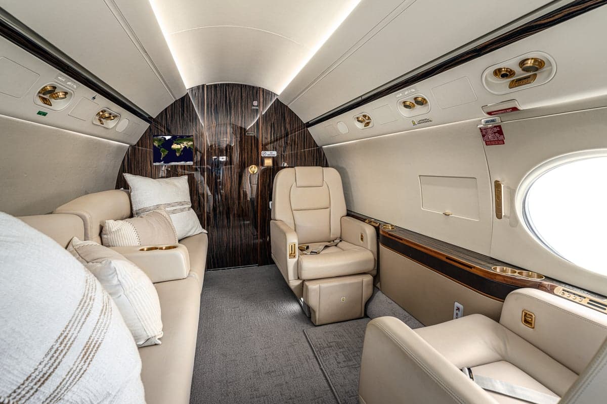 The interior of the aircraft features a couch with pillows and cream-colored leather seats.