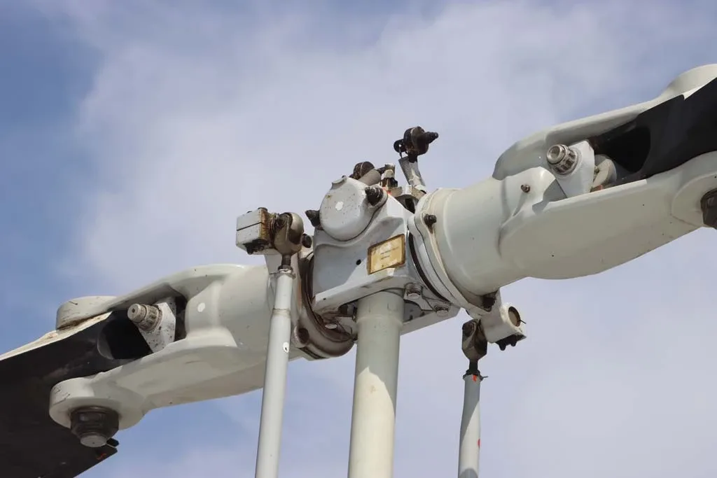 Close-up view of the main rotor head assembly of a helicopter against a blue sky.