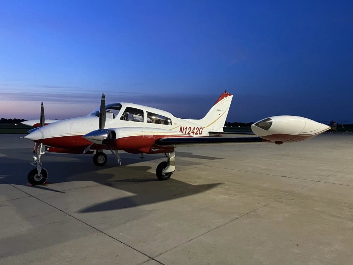 The N1242G twin-engine aircraft with red and white paint scheme, parked on an airfield at night.