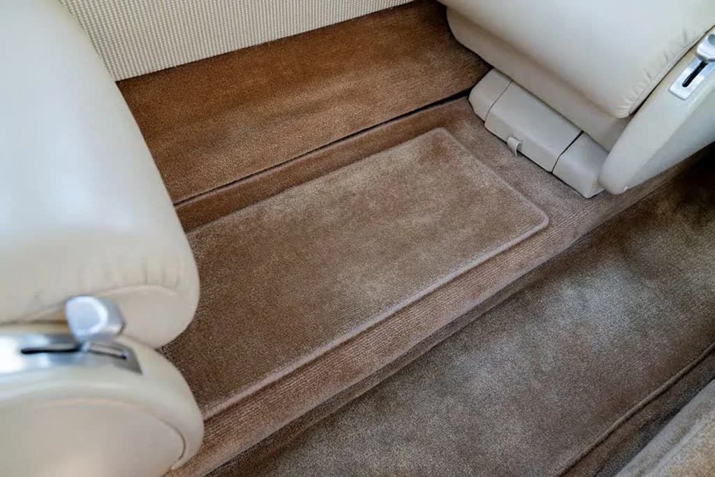 A close-up view of the brown carpeted floor and footwell between seats in the private jet's cabin.