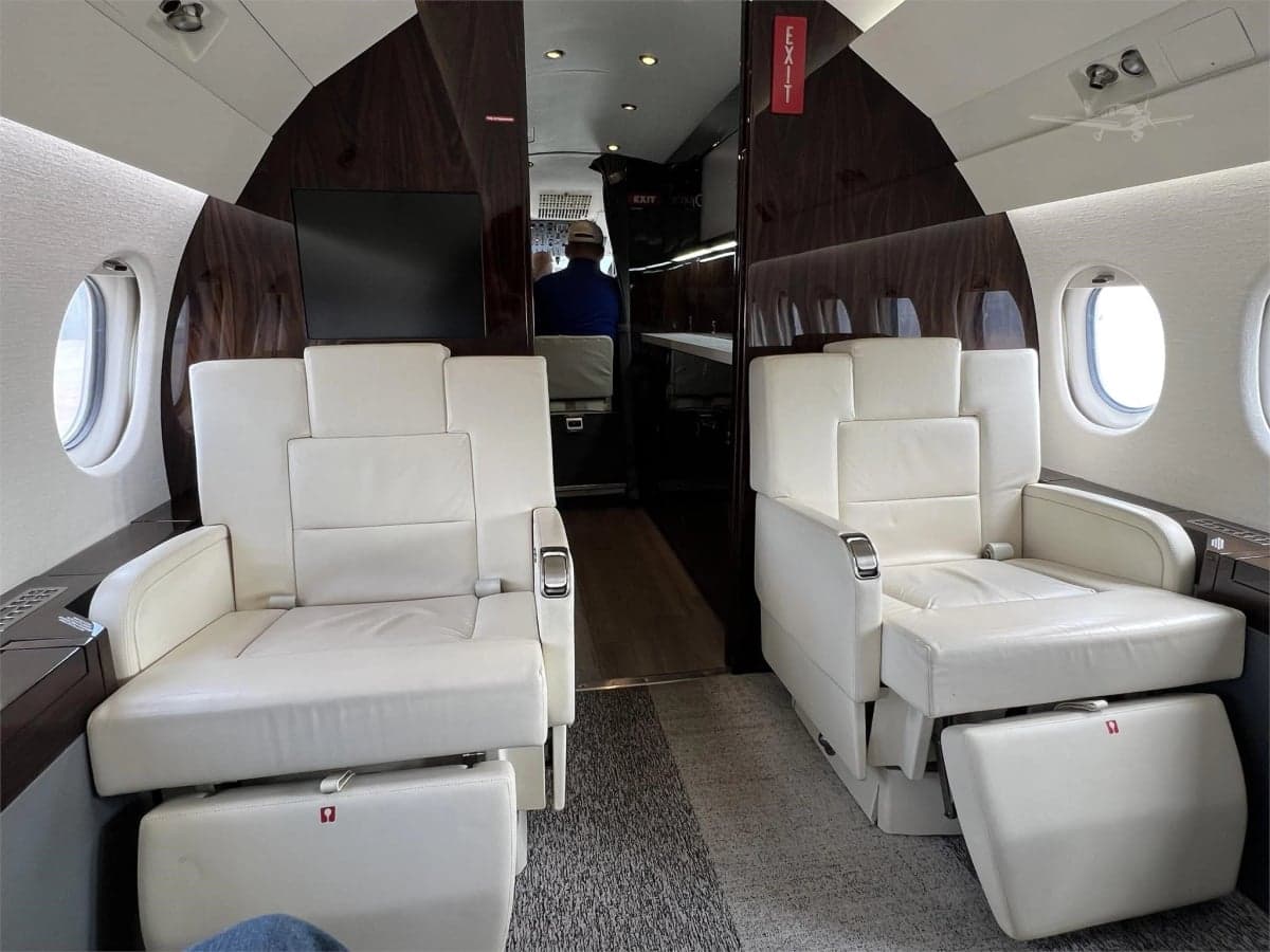Interior view of the aircraft cabin with cream-colored leather seats and a dark wood accent wall.