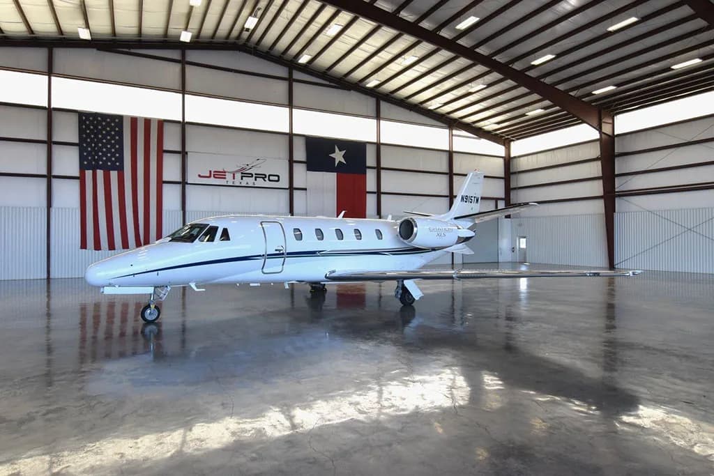 A white Cessna Citation XLS business jet with blue and silver stripes, tail number N915TM, parked inside a hangar.
