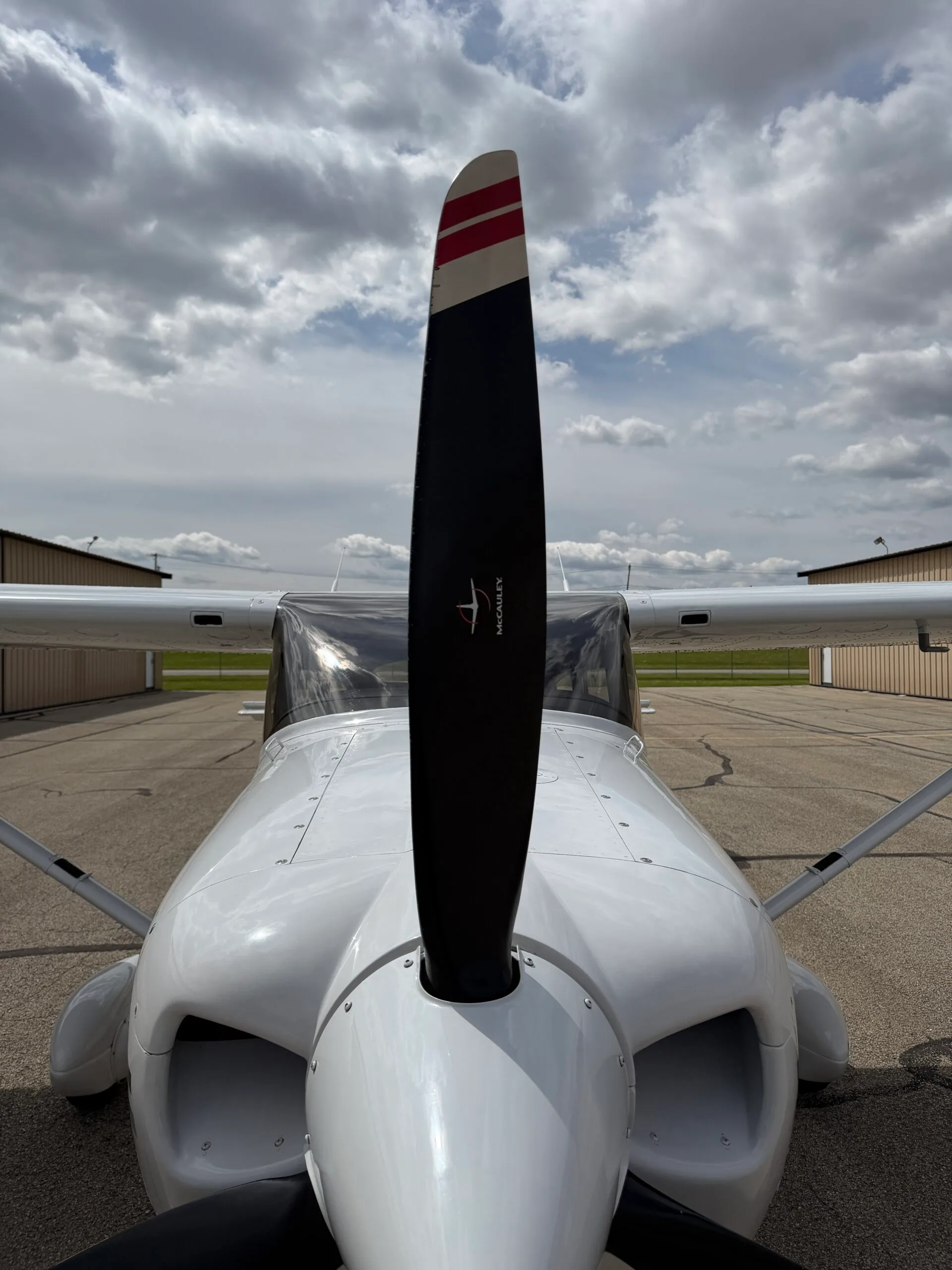 A head-on view of the aircraft's propeller and nose, with hangars in the background.